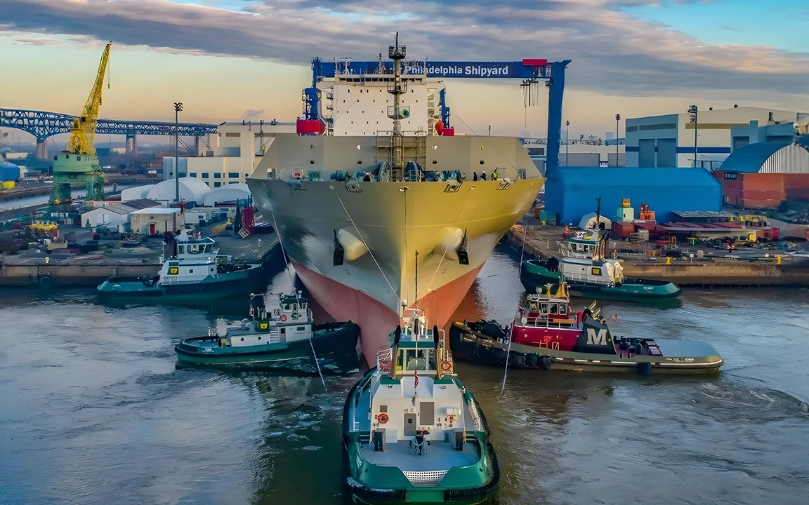 A large vessel is maneuvered by tugboats at Philly Shipyard during launch operations.