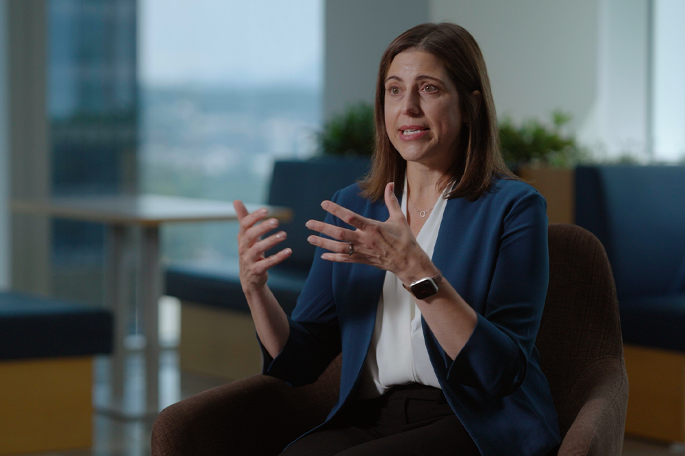 Danielle Merfeld sitting in a chair, gesturing with both hands while speaking about solar energy.