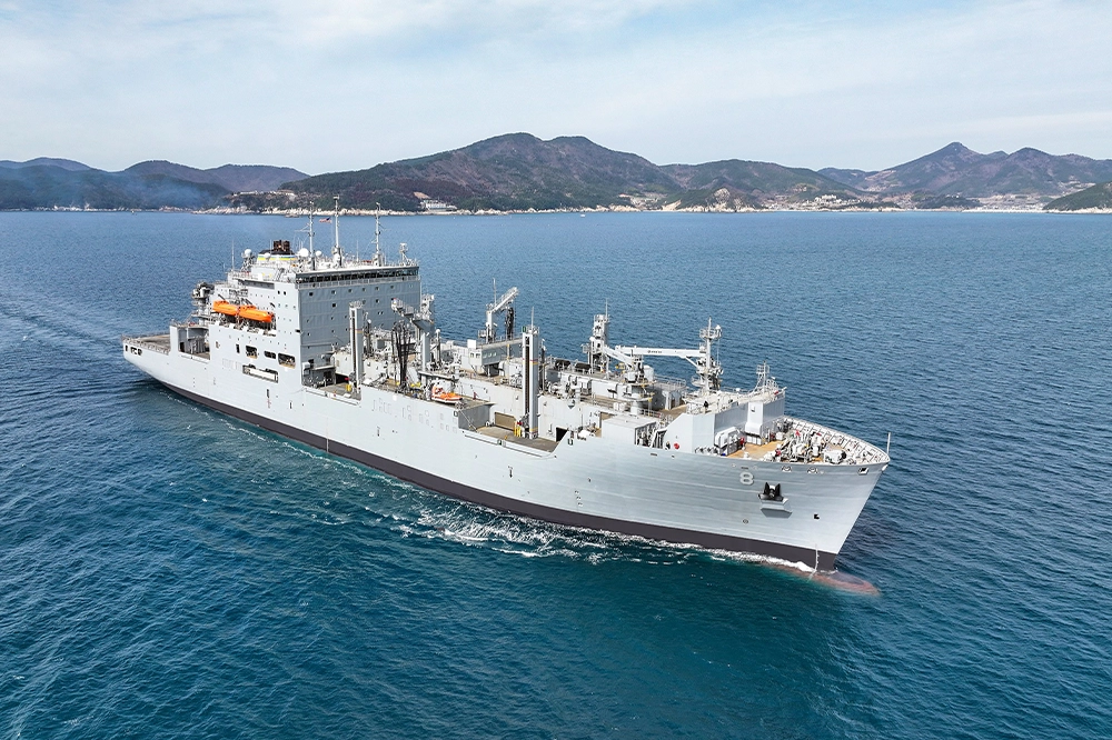 USNS Wally Schirra sailing on a partly cloudy day with a landmass in background