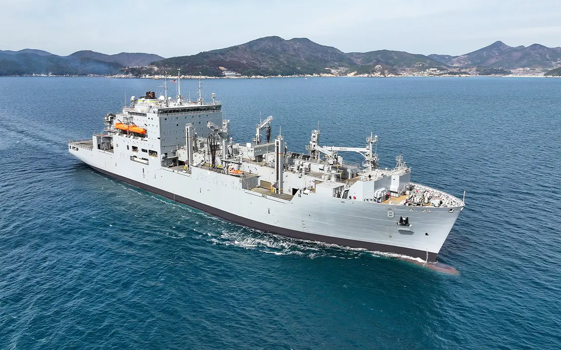 USNS Wally Schirra sailing on a partly cloudy day with a landmass in background